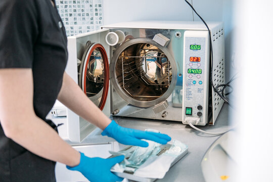 Person prepares dental instruments in packaged pouches near open autoclave sterilizer machine. Autoclave sterilization process, medical instrument sterilizer, dental tool sterilization technology.