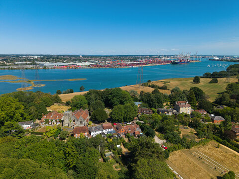 Aerial view of St Mary's Church and the historic village of Eling, surrounded by lush greenery, with the River Test and Southampton Docks in the background in Eling, England, United Kingdom.