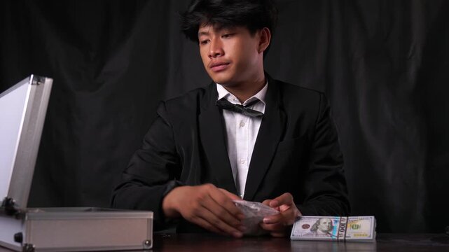Confident mafia boss in a tuxedo unpacks bags of illegal white powder from a briefcase next to stacks of cash. Concept of a drug cartel exchange, narcotics trafficking, and organized crime.
