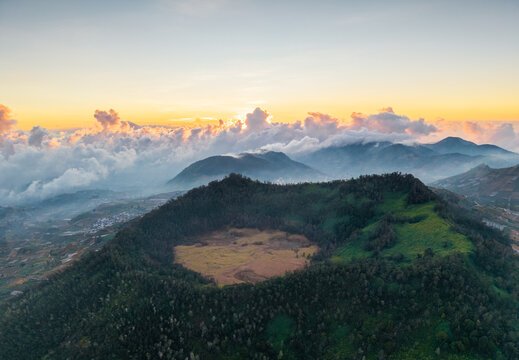 Aerial view of the volcanic crater at Dieng Plateau with lush green slopes and clouds illuminated by the golden hour sunset in Indonesia.