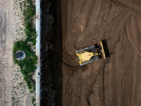Aerial view of a yellow bulldozer leveling soil at a construction site next to a concrete retaining wall in Kaunas, Kaunas County, Lithuania.