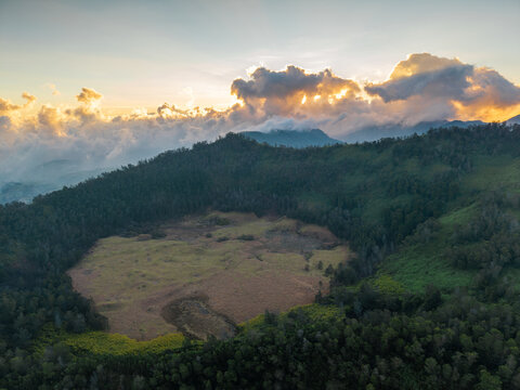 Aerial view of Dieng Plateau featuring a volcanic crater surrounded by lush green forests under a golden sunset sky in Indonesia.