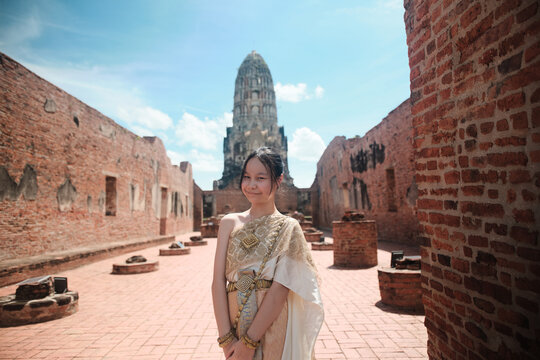 Portrait of Asian teenage girl dressed in Thai traditional outfit with cheerful smile and looking at camera, holiday travel in Ayutthaya, Southeast Asia, ancient ruins heritage,  tourist destination.