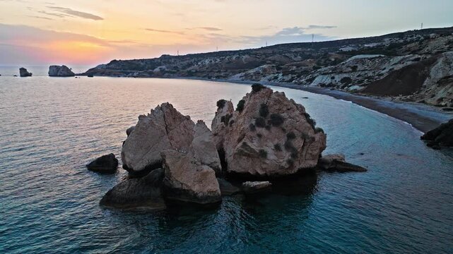 Drone view of Aphrodite&rsquo;s Rock at golden sunset at Petra tou Romiou in Cyprus. The iconic sea stack, surrounding rocks and calm blue sea create a beautiful coastal landmark scene.