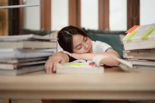 College Asian teenage girl tired and burned out from overwhelmed study pile of books, stressed learning at home with pile of textbooks, reading and writing for school exam, homeschooling education.