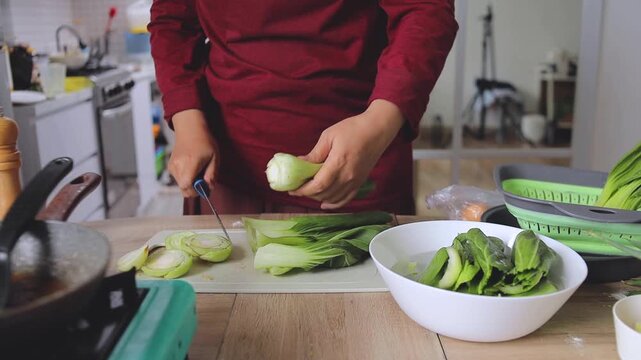 Chef slicing fresh bok choy green vegetables on cutting board with knife in home kitchen
