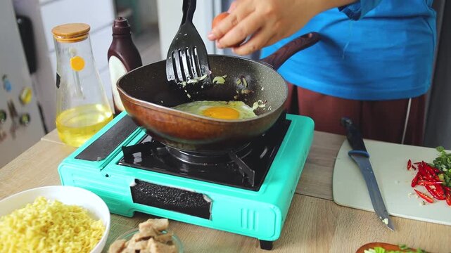 Chef frying egg with chopped shallots and garlic in skillet during meal preparation