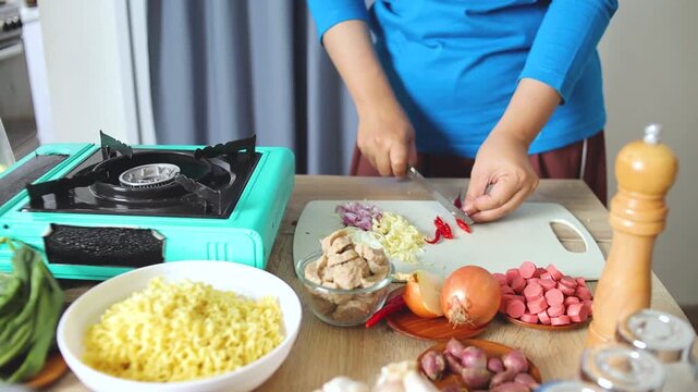 Kitchen scene showing hands slicing chili peppers on cutting board