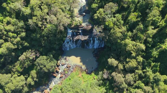 Multi-tier waterfall surrounded by dense Upper Paran&aacute; Atlantic Forest near Lago Urugua-i, Misiones, Argentina, highlighting pristine subtropical rainforest, Top-down drone forward flyover reveal