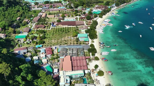 Phi Phi Don beach and harbor with turquoise sea and boats, drone establishing backdrop from hillside along bent coastline