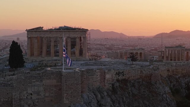 Drone view of the Acropolis on a national day of mourning, with the Greek flag waving at half mast, creating a solemn and respectful atmosphere over historic Athens.