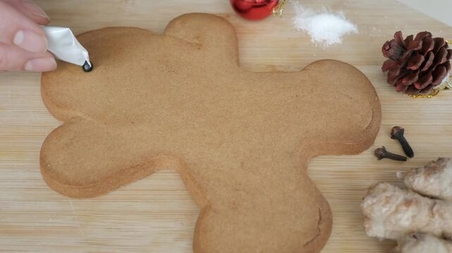Blank large gingerbread cookie on wooden board being decorated with coloured icing. Spices and seasonal decoration nearby