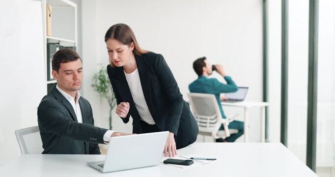 Portrait of male manager shows data on laptop to woman colleague in office. Businesspeople monitor project realization stages on computer in corporate workplace