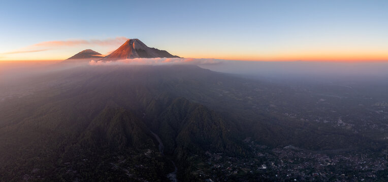 Aerial view of Mount Merapi at sunset with volcanic slopes, clouds, and lush greenery in Pakem, Special Region of Yogyakarta, Indonesia.