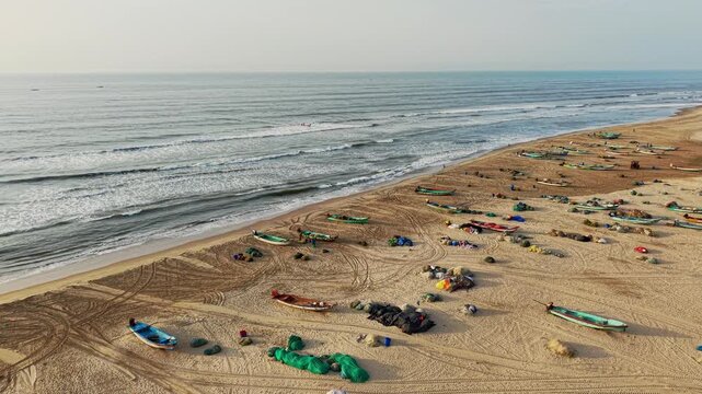 Aerial drone shot of fishing boats resting on Chennai beach as Bay of Bengal waves roll onto the sandy shoreline lined with fishing nets in Tamil Nadu, India
