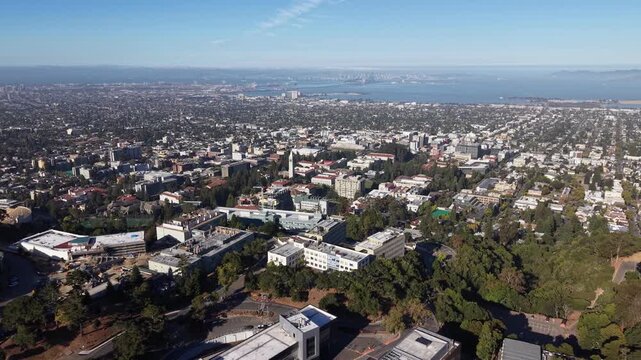 Expansive aerial view slowly revealing the University of California, Berkeley campus, with the cityscape, San Francisco Bay, and the iconic Bay Bridge visible in the sunny, hazy background