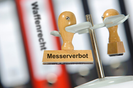 Ein Holzstempel ist beschriftet mit dem Aufdruck: Messerverbot vor einem Aktenordner mit der Aufschrift Waffenrecht