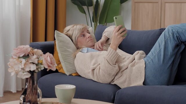 Mature woman using a smartphone while lying on a couch