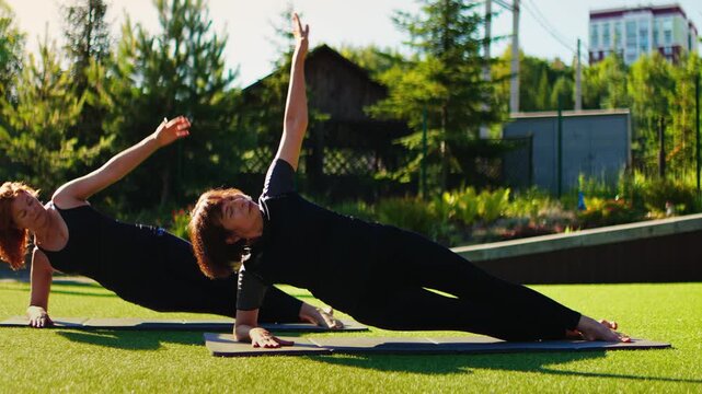 Elderly women practicing slow motion Pilates side plank exercises together outdoors on yoga mats, focusing on core strength, balance, and graceful senior fitness