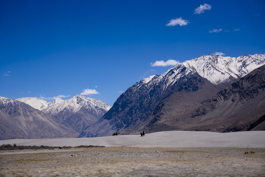 View of the snow-capped Himalayan mountains rising above the vast desert landscape of the Leh valley under a clear blue sky in Leh, Ladakh, India.