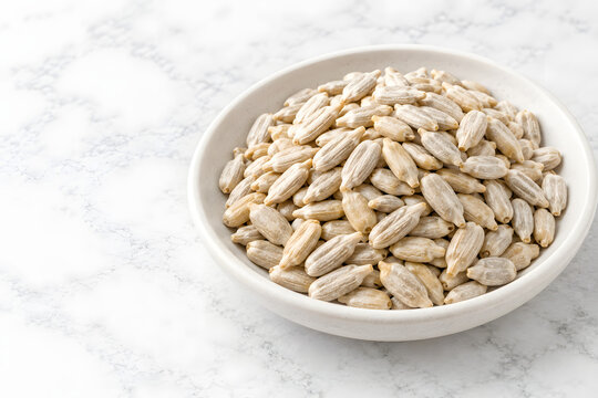 Raw peeled sunflower seed kernels piled inside a shallow matte-white ceramic dish on marble