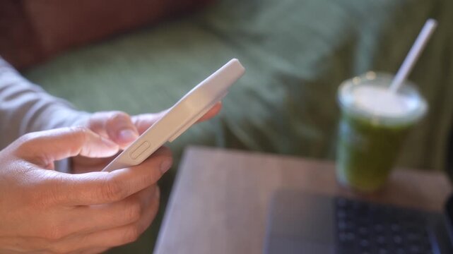 Smartphone Messaging In Morning Living Room, Close Up Hands Typing On Mobile Phone Beside Laptop And Green Tea Drink, Remote Work,Digital Communication, Business Lifestyle. Home Office Productivity.