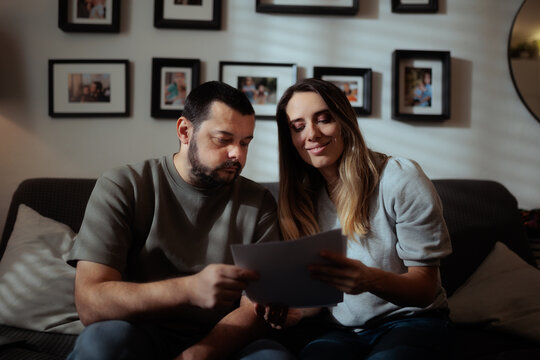 Happy Wife And Husband Reading Financial Contract Agreement Together Indoors. Smiling married couple happily reviews their official real estate mortgage house buying contract