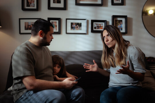 Stressed Little Girl Cringes Near Father During Intense Parents Argument. Anxious child crouches beside her dad during a stressful loud parental marriage argument