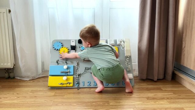Toddler twisting locks and latches on sensory board. Age appropriate learning toy. Child discovering how everyday objects work. Motor skills training while having fun