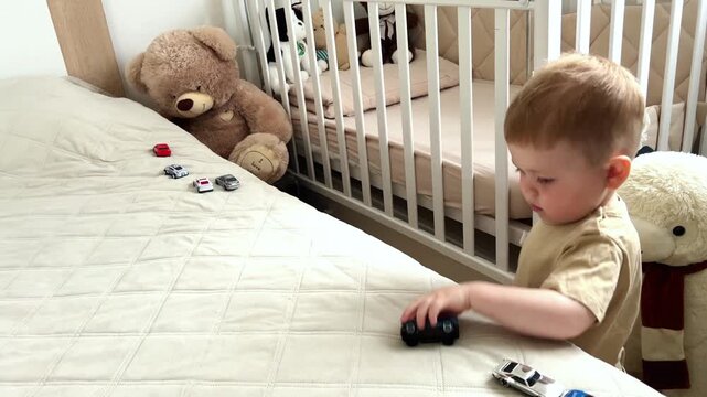 Little boy moving toy cars on soft bed surface. Imitating engine sounds. Masculine interests at childhood. Play developing motor skills and storytelling
