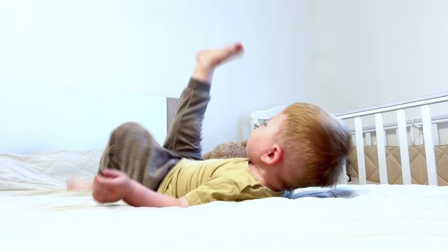 Caucasioan baby in playful pose, playing on soft white bed, happy smile, chubby cheeks. Pure joy and playful spirit
