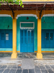 Fototapeta premium Colorful facade of traditional shophouse architecture with vibrant blue shutters and yellow columns in Hoi An Ancient Town, Vietnam
