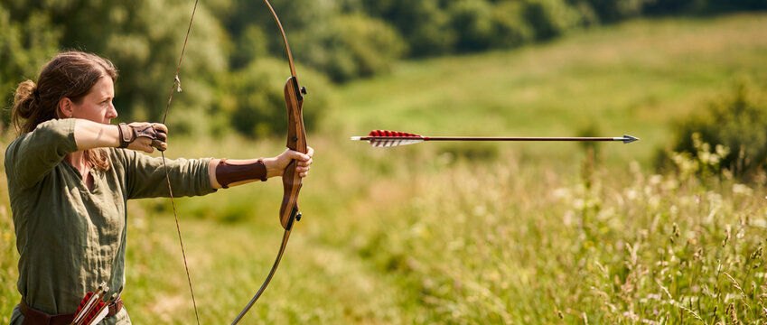 Female archer drawing bow and releasing arrow during outdoor archery practice in countryside field