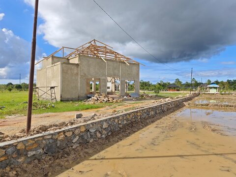 House building under construction with wooden roof frame in rural area under cloudy sky