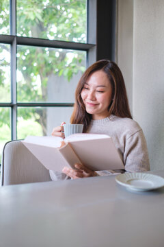 Vertical portrait image of a woman reading a book and drinking coffee