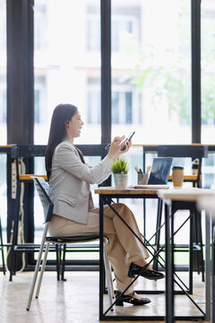 Professional businesswoman smiling while using smartphone and stylus pen in a modern office co working space