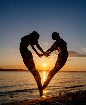 Two white women doing partner acrobatics yoga at sunset on a beach