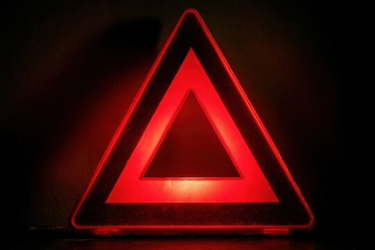 Red emergency reflective warning triangle on a dark surface for road safety alert