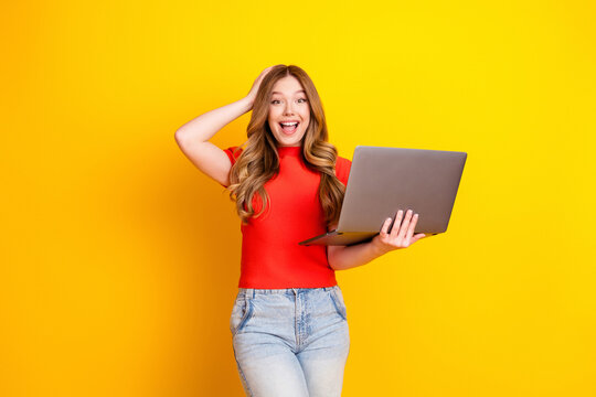 Surprised young woman holding laptop and smiling on yellow background, remote work and online learning technology concept