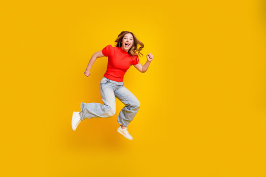 Young woman jumping with joy in a red top and jeans on a bright yellow background, energetic lifestyle portrait celebrating freedom, happiness and positive youth energy