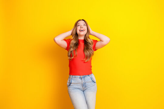 Happy young woman in red shirt looking up and smiling against a bright yellow background, casual portrait conveying joy, optimism and playful energy