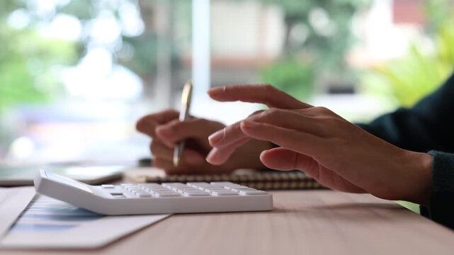 Close-up of businesswoman calculating finances, analyzing business data, and taking notes on a notepad while working on financial reports at her office desk