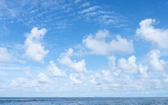 Blue Sky Background With White Clouds Over Summer Sea, Calm Ocean Horizon And Bright Daylight, Tropical Weather, Coastal Nature Landscape, Travel Season, Panoramic Cloudscape And Seascape.