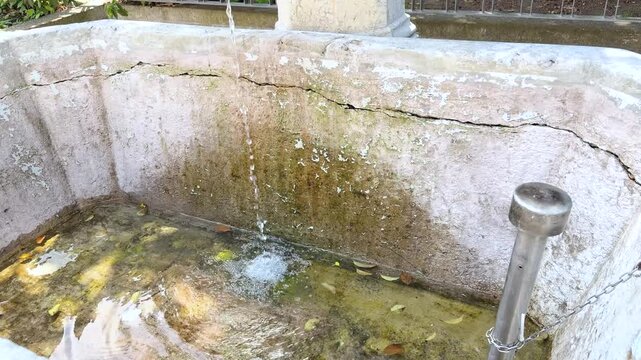 A weathered concrete fountain in L&ouml;rrach, Germany, gradually fills with fresh water flowing into the basin. Moss-covered walls. High-angle tilt up shot