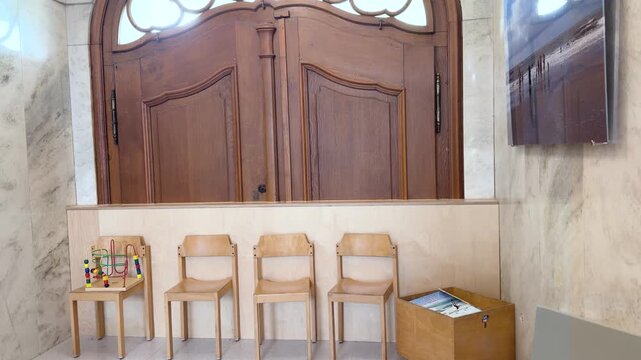 A tilt-up shot begins with a children's wire bead maze in the corner of a hospital waiting area before revealing rows of waiting chairs and the elegant historic architecture. Tilt up shot.
