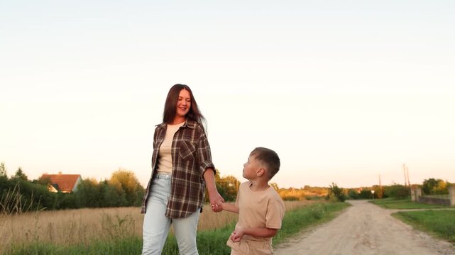 Happy mother and son walk hand in hand along sandy path through countryside. Slow motion shows playful moments as mother puffs cheeks and child laughs with joy.