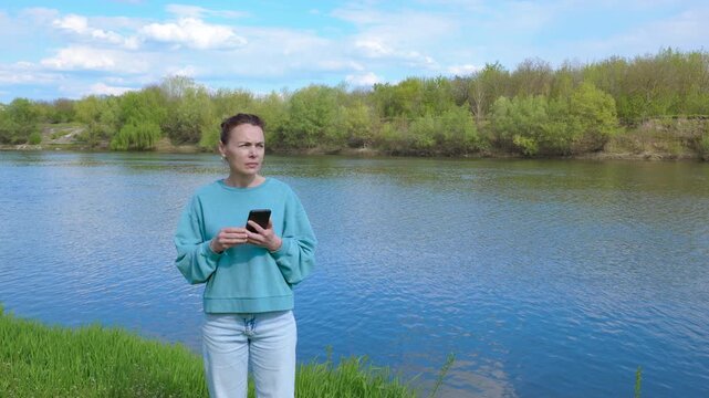 Woman by the river uses a map on her smartphone. Caucasian woman searches for a map on her smartphone, then finds a route and leaves