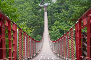 Fototapete Bordeaux Gamaksan Suspension Bridge stretching across a lush forest valley on Gamaksan Mounta in Paju Gyeonggi-do, South Korea, beneath a bright blue sky.  © WASAN