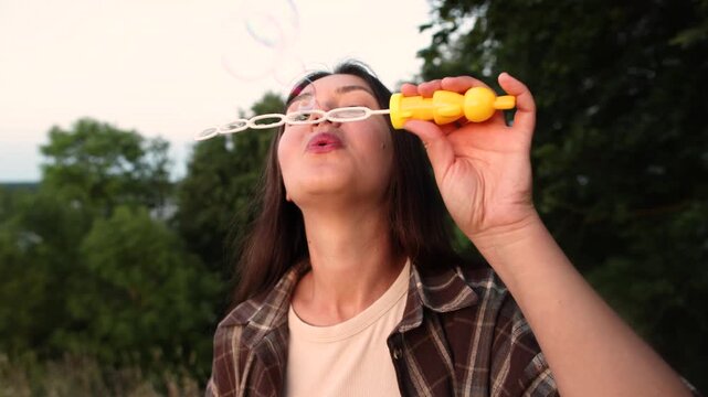 Young woman blows soap bubbles outdoors during evening light. Slow motion captures beauty relaxation and playful summer mood with dreamy atmosphere.
