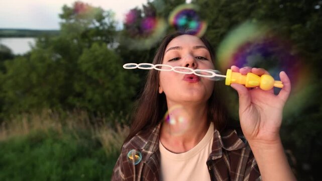 Young woman blows soap bubbles outdoors during evening light. Slow motion captures beauty relaxation and playful summer mood with dreamy atmosphere.